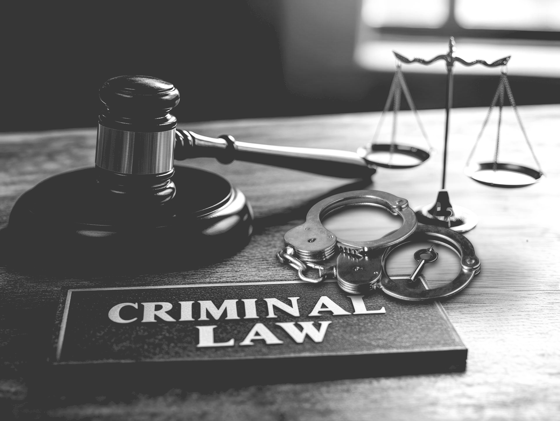Gavel, cuffs, and scales on desk symbolizing justice and criminal law.