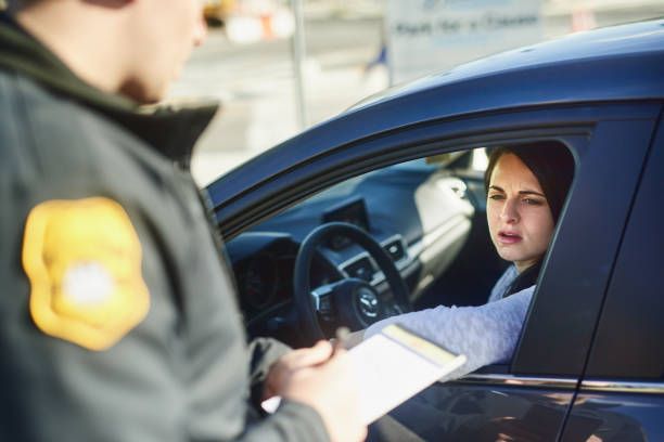 A police officer is writing a ticket to a woman in a car.