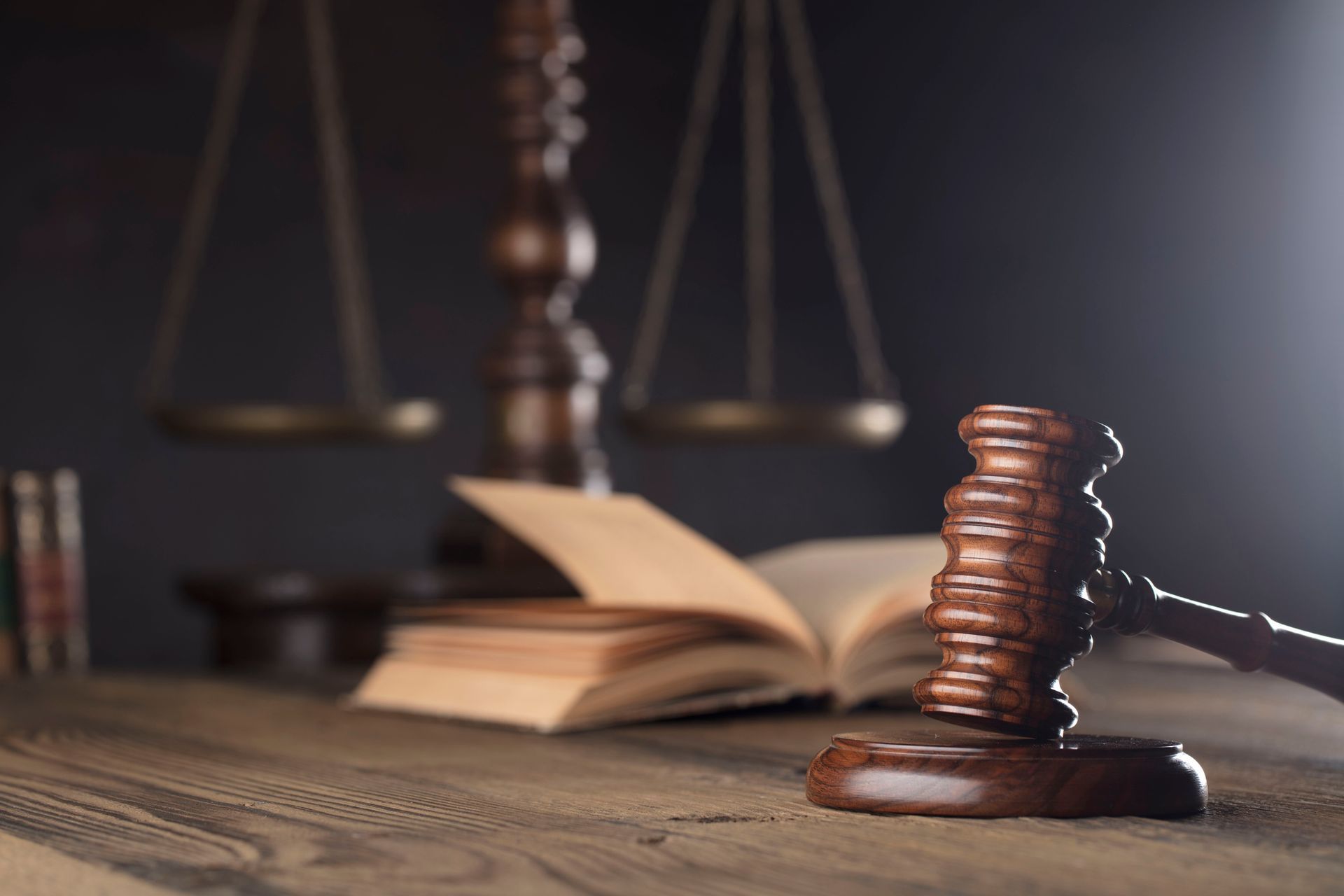 Wooden gavel, scales of justice, and open law book on a wooden desk.