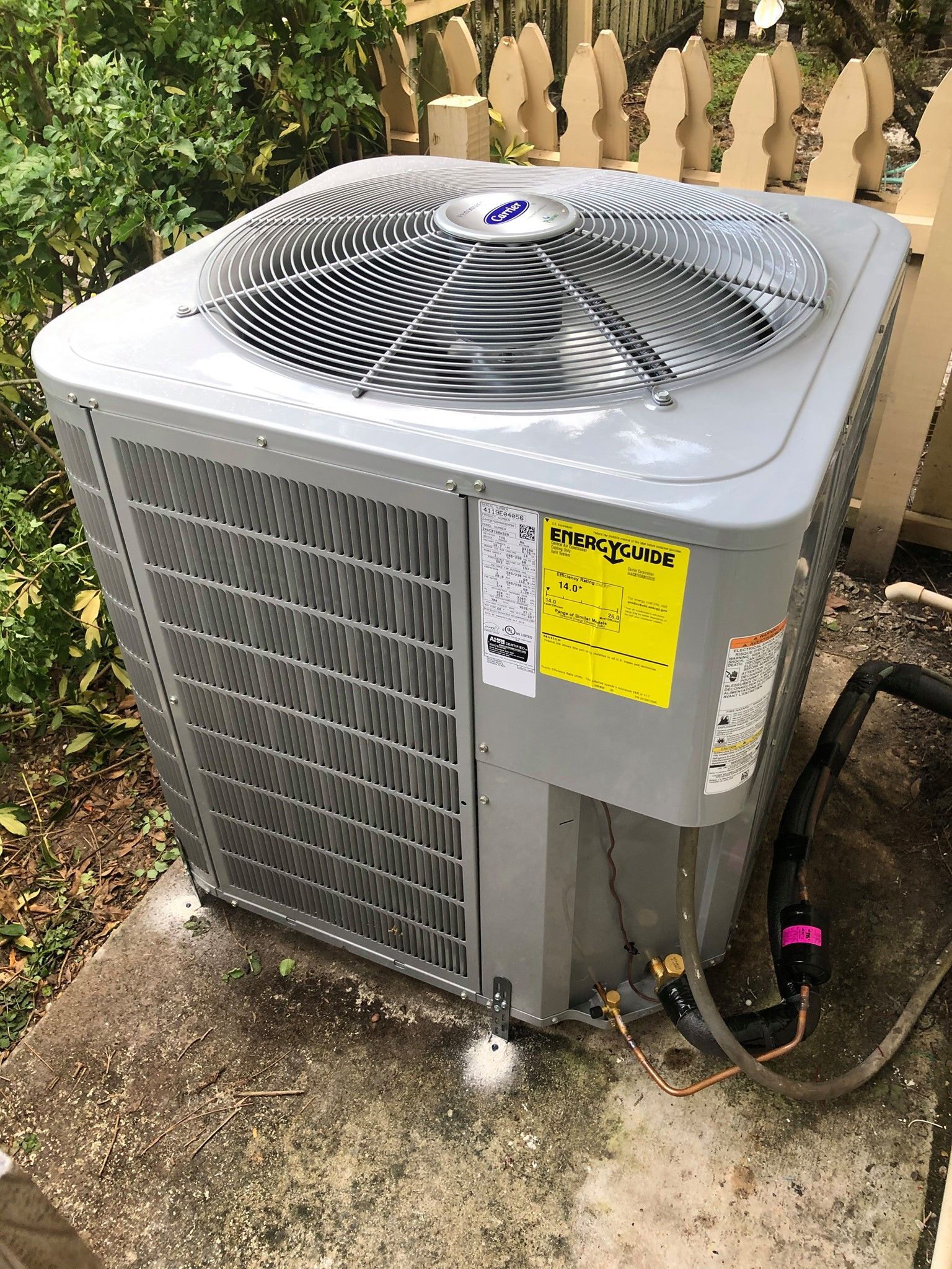 A large air conditioner is sitting on the ground next to a fence.