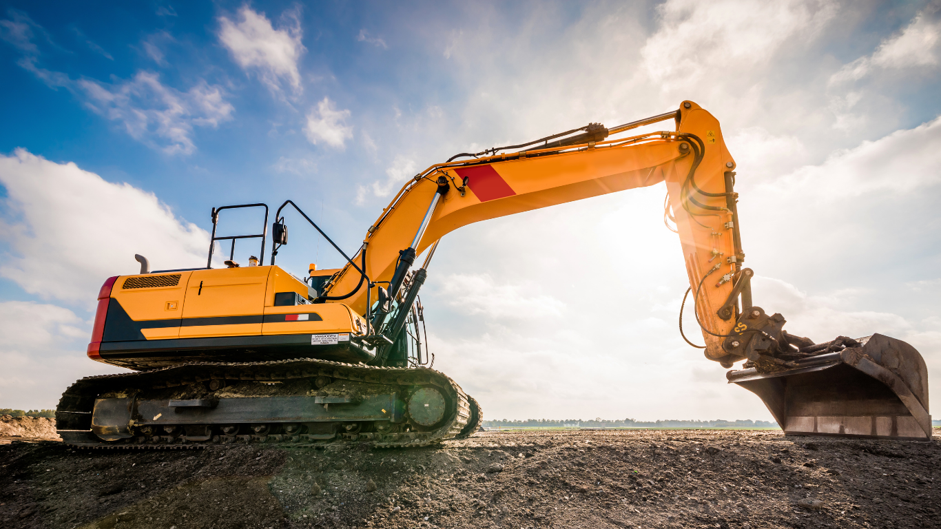 A yellow excavator is sitting on top of a dirt field.