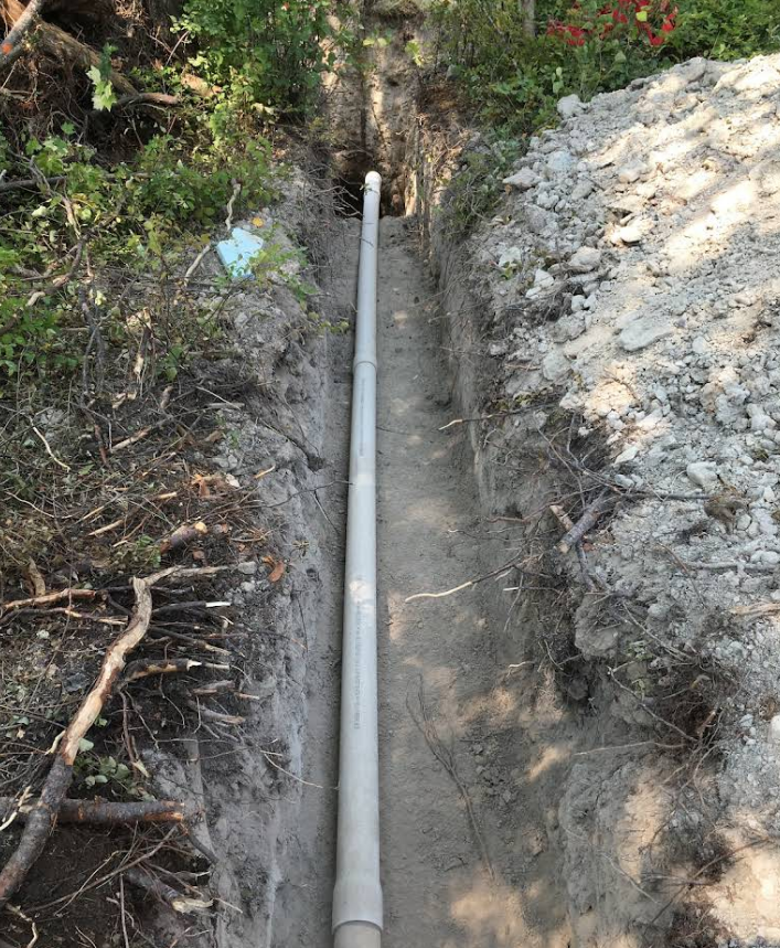 A white pipe is laying in the dirt in a trench.