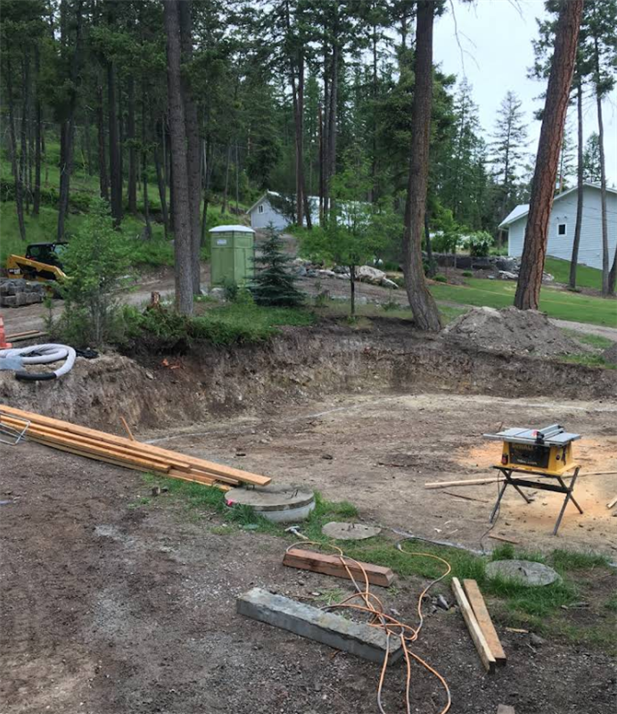 A wooden table is sitting in the middle of a dirt field surrounded by trees.