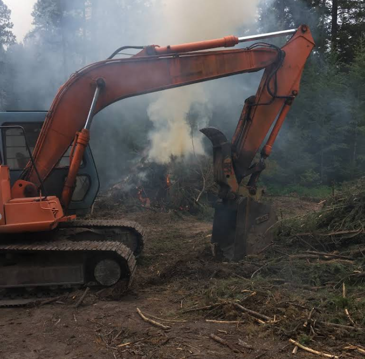 A large orange excavator is working in a field with smoke coming out of it