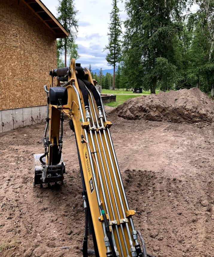 A yellow excavator is sitting in the dirt in front of a house.