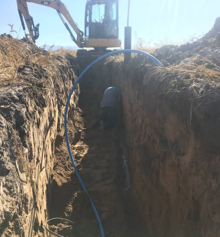 An excavator is digging a trench with a blue hose attached to it