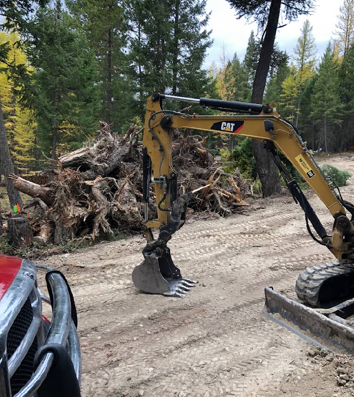 A cat excavator is digging in the dirt near a pile of logs.