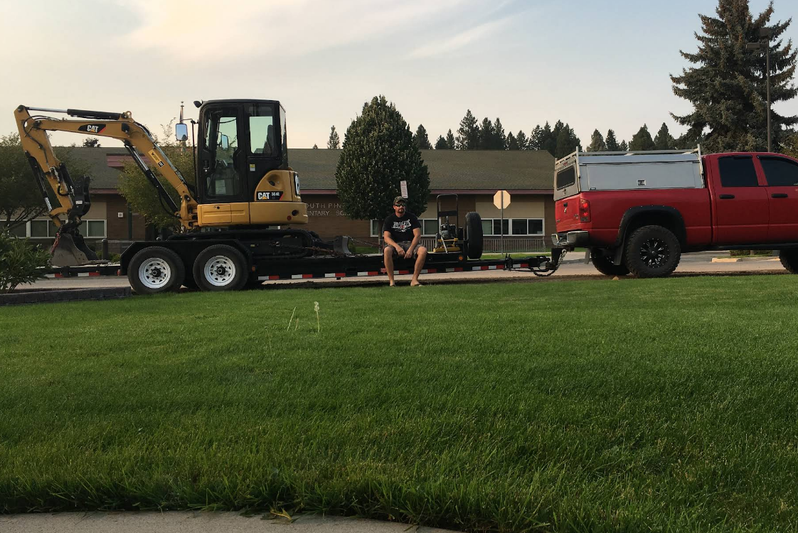 A red truck is towing a yellow excavator on a trailer.