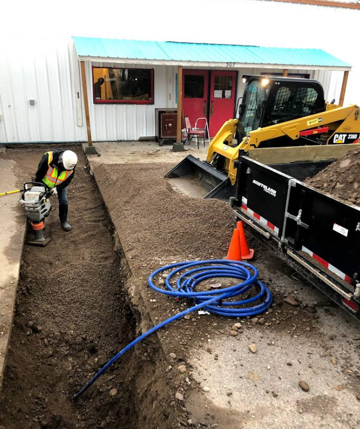 A construction worker is digging a trench in front of a building.