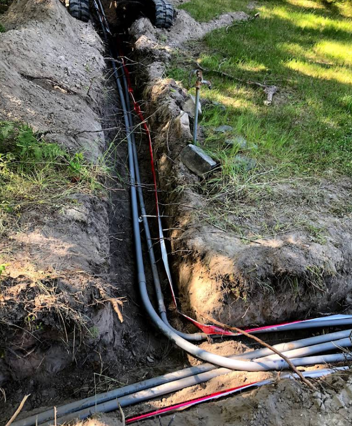 A person is digging a trench with electrical wires coming out of it.