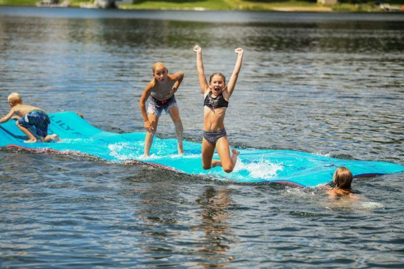 A group of children are playing in the water on a floating mat.