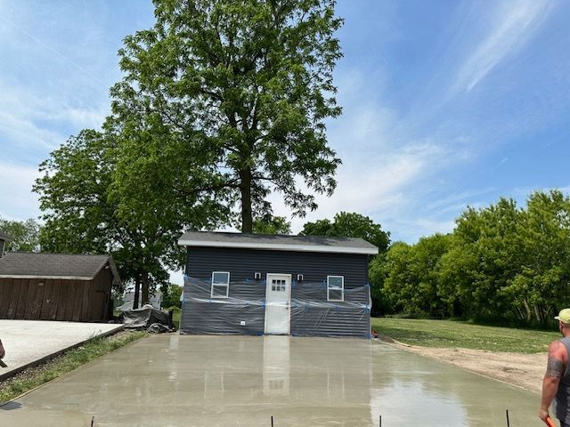 A man is standing in front of a small house with a tree in the background.