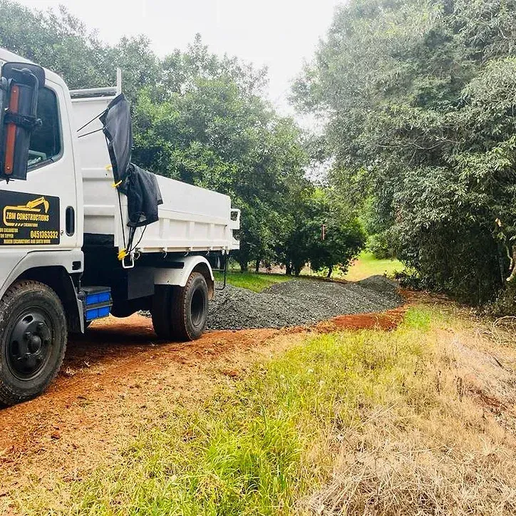 A White Dump Truck Is Parked Next to A Red Excavator on The Side of The Road — ZBM Constructions in Wollongbar, NSW