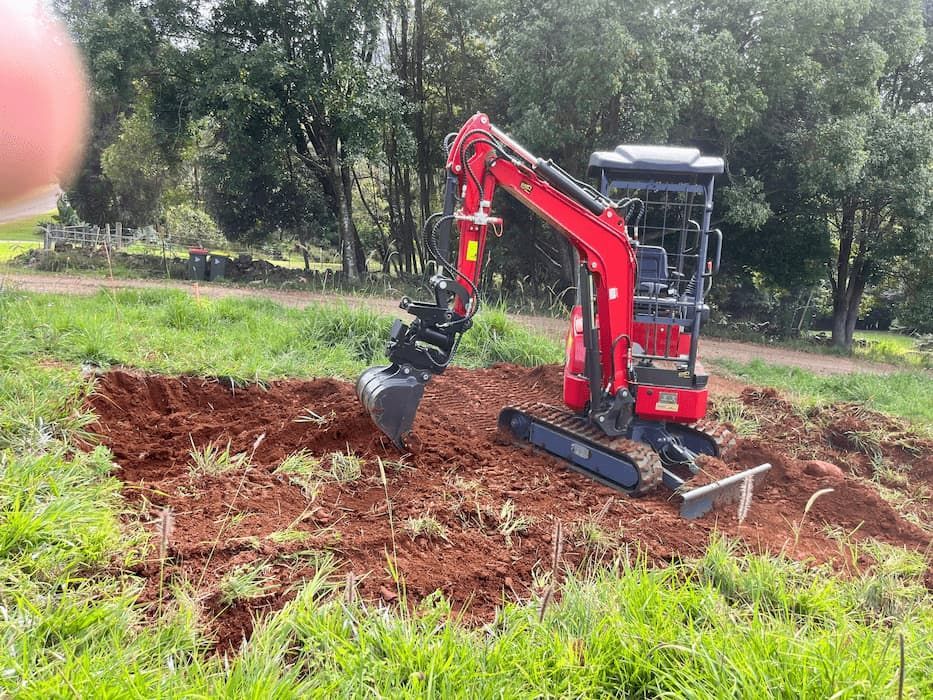 A red excavator is digging a hole in a field — ZBM Constructions in Wollongbar, NSW