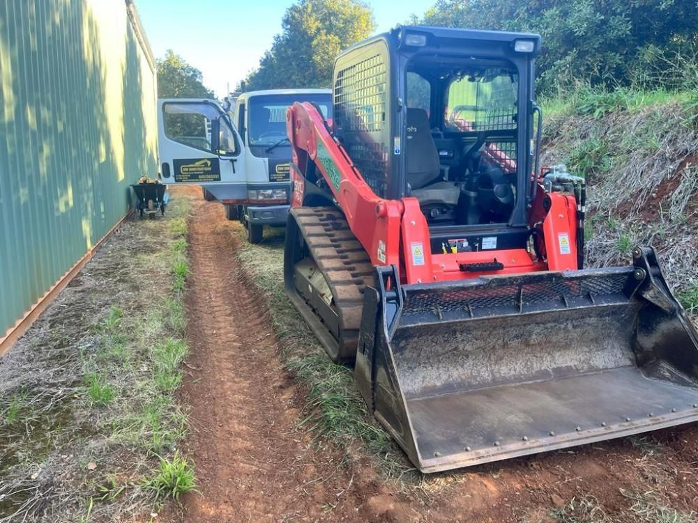 A Red Bulldozer Is Parked on A Dirt Road Next to A White Truck — ZBM Constructions in Wollongbar, NSW