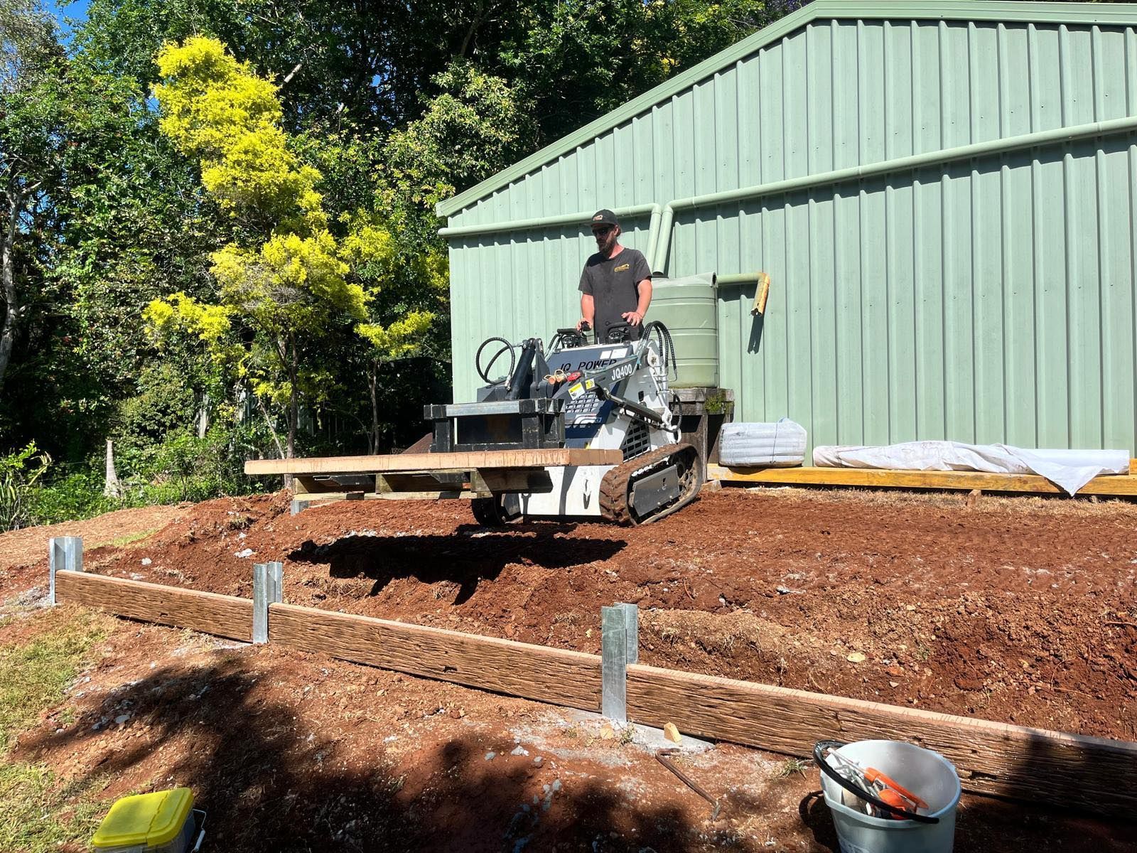 A man is standing next to a machine that is moving dirt — ZBM Constructions in Wollongbar, NSW