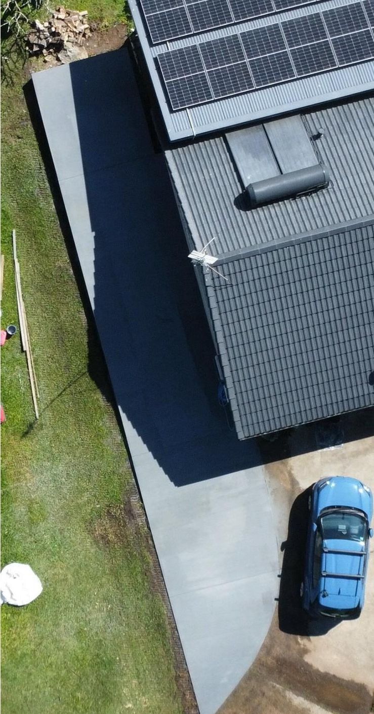 An aerial view of a house with solar panels on the roof and a blue car parked in front of it.