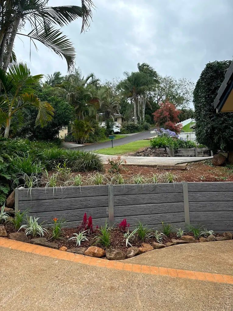 A wooden retaining wall with flowers and trees in front of a house — ZBM Constructions in Wollongbar, NSW