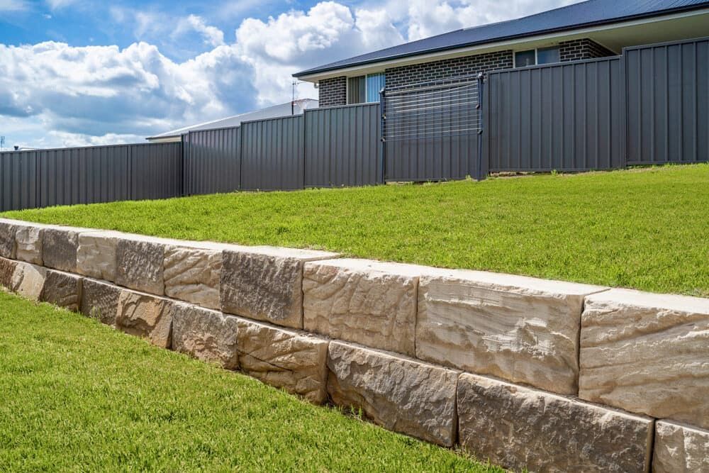 A Stone Wall Surrounds a Lush Green Lawn in Front of a House — ZBM Constructions in Alstonville, NSW