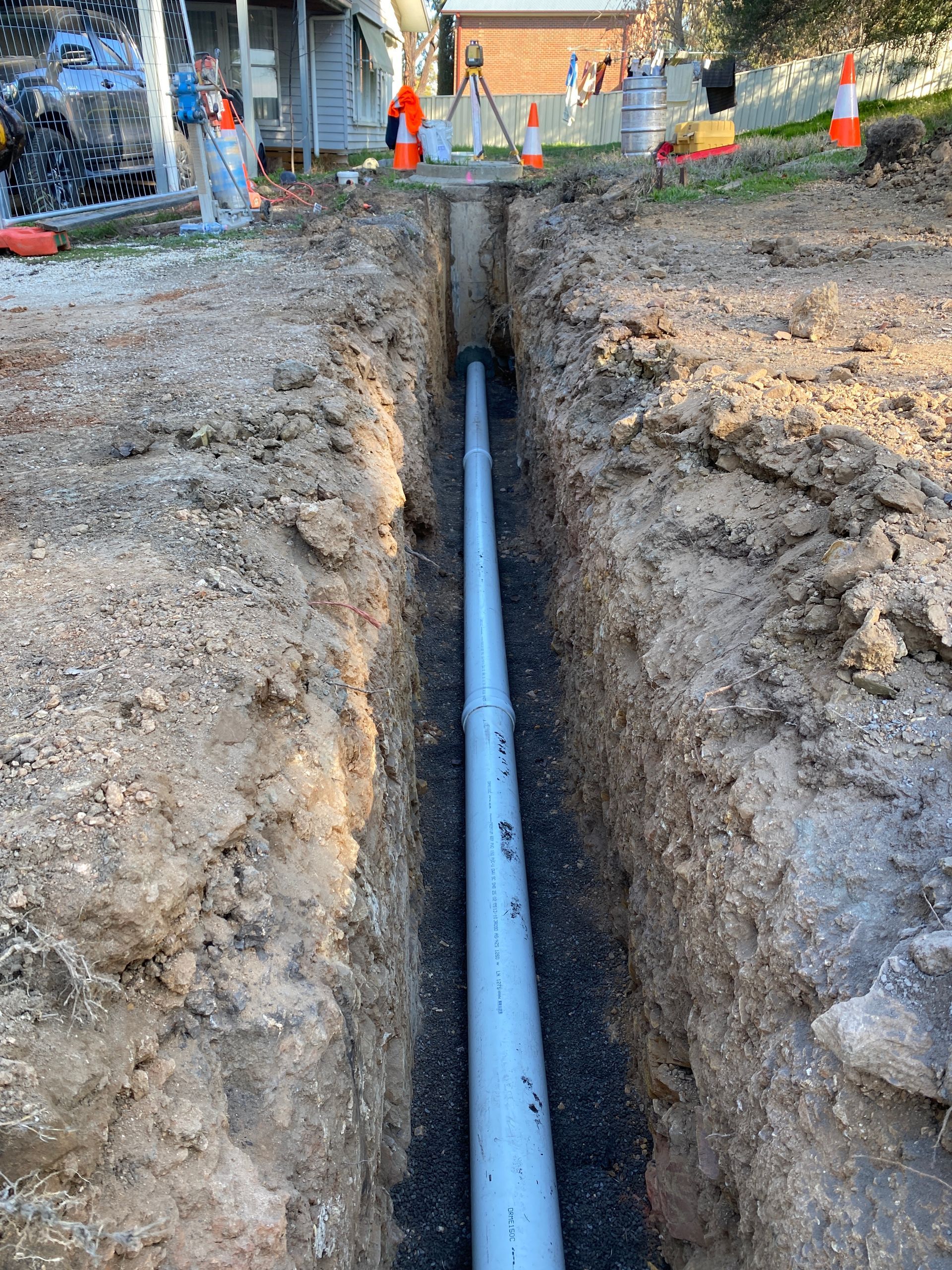 A pipe is being installed in the dirt next to a fence.