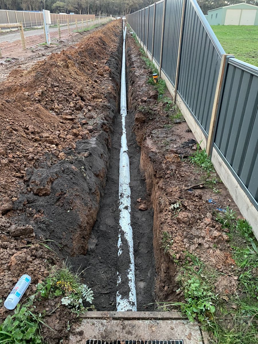 A pipe is being installed in the dirt next to a fence.