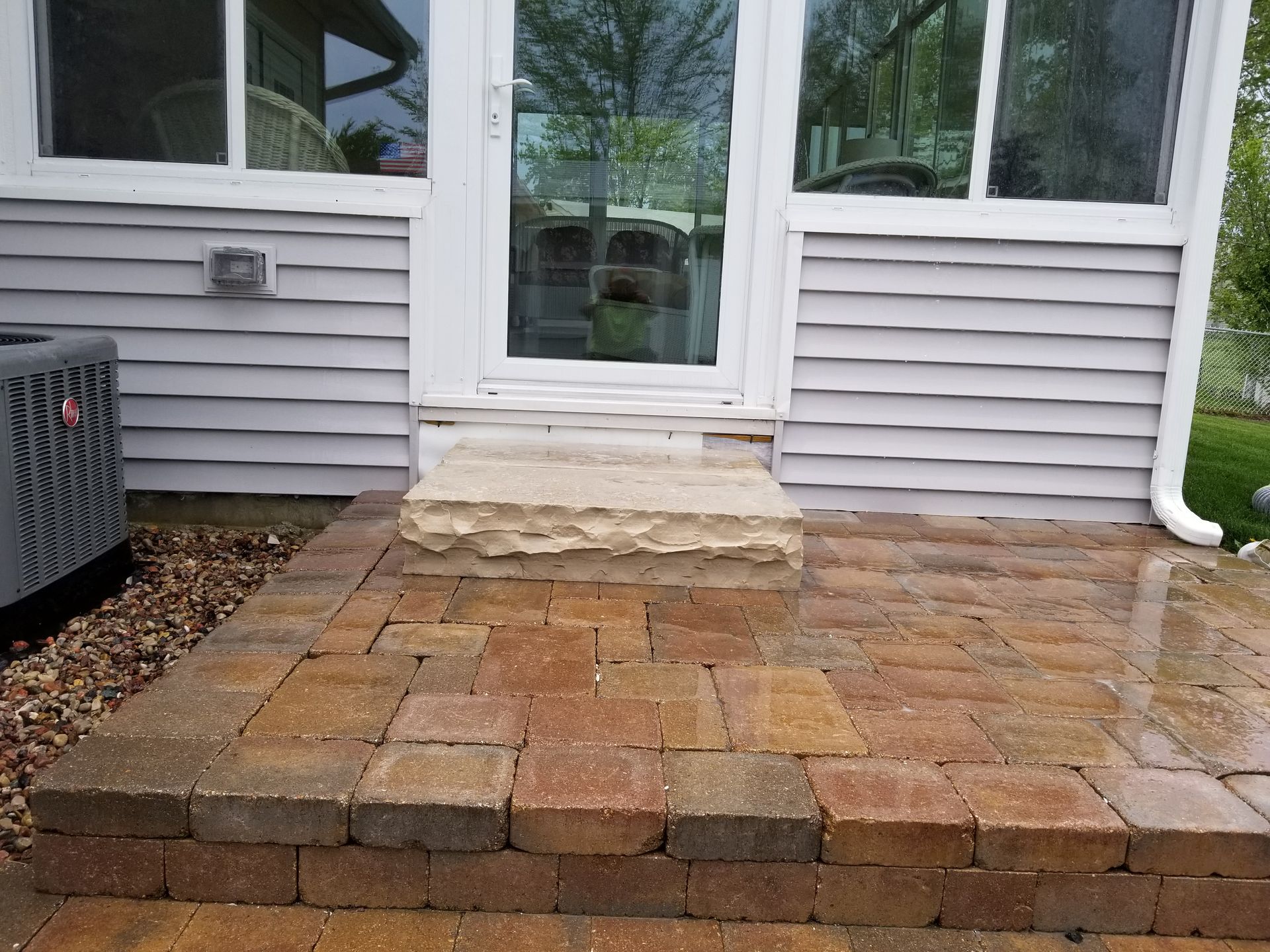 Brick patio steps leading up to a door with glass panels; gray siding on the house.