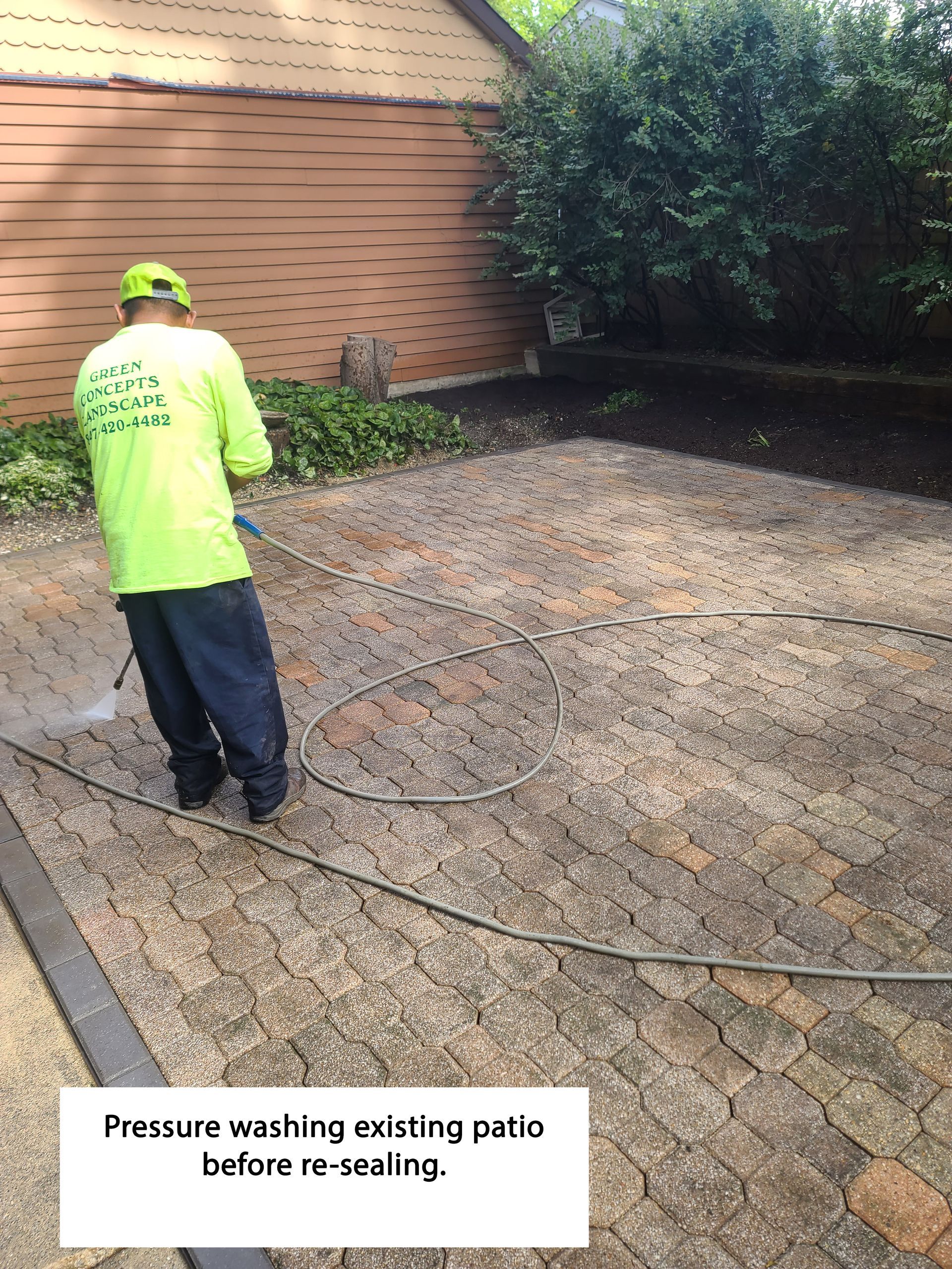 Man power washing a brick patio before re-sealing, in a yard.