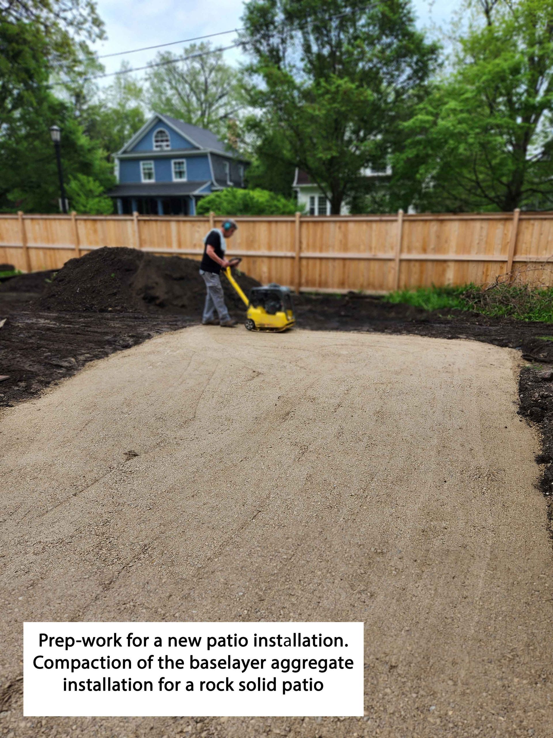 Person compacting gravel base for patio installation.