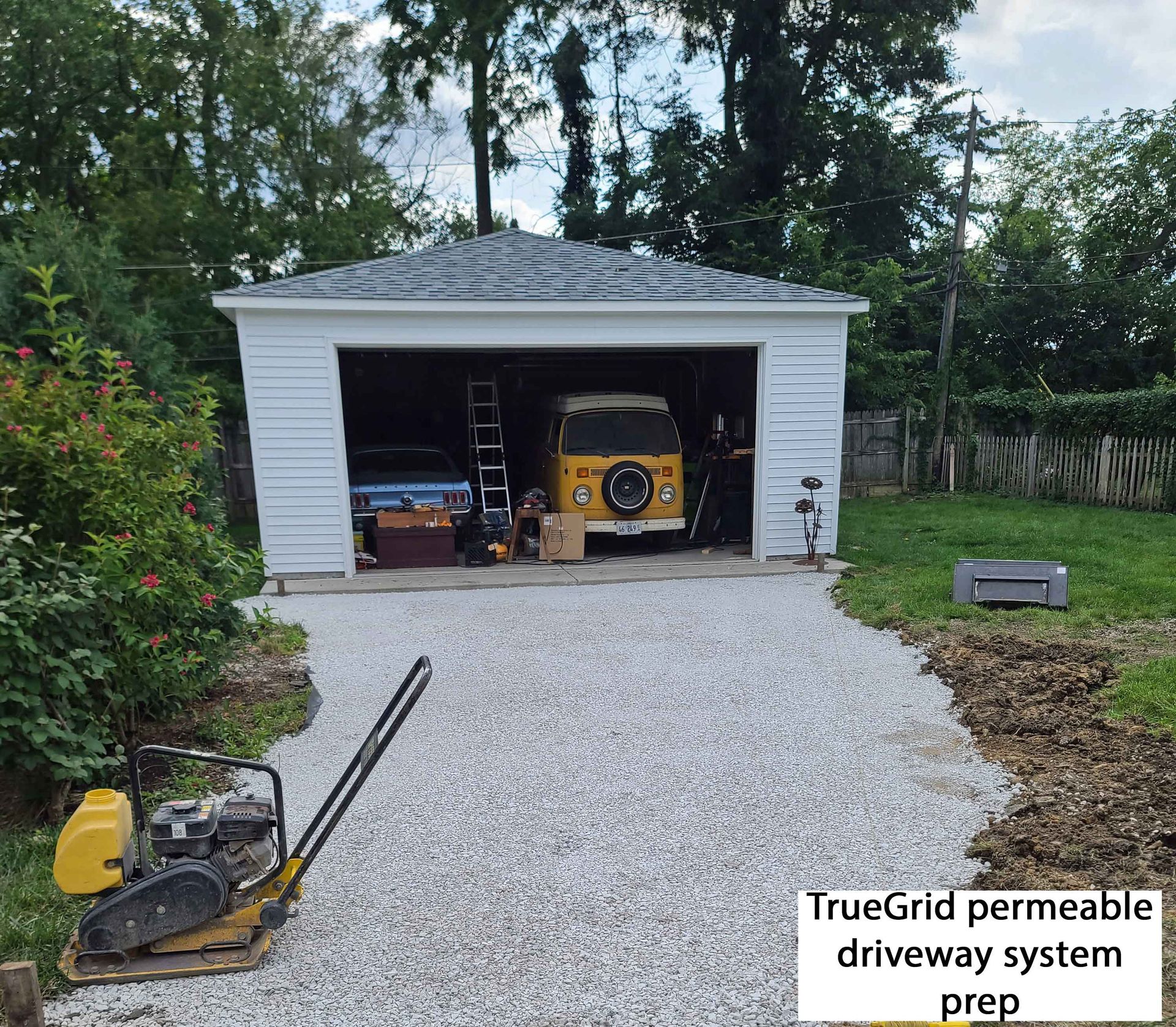 Garage with a yellow van inside, gravel driveway prep with compactor.