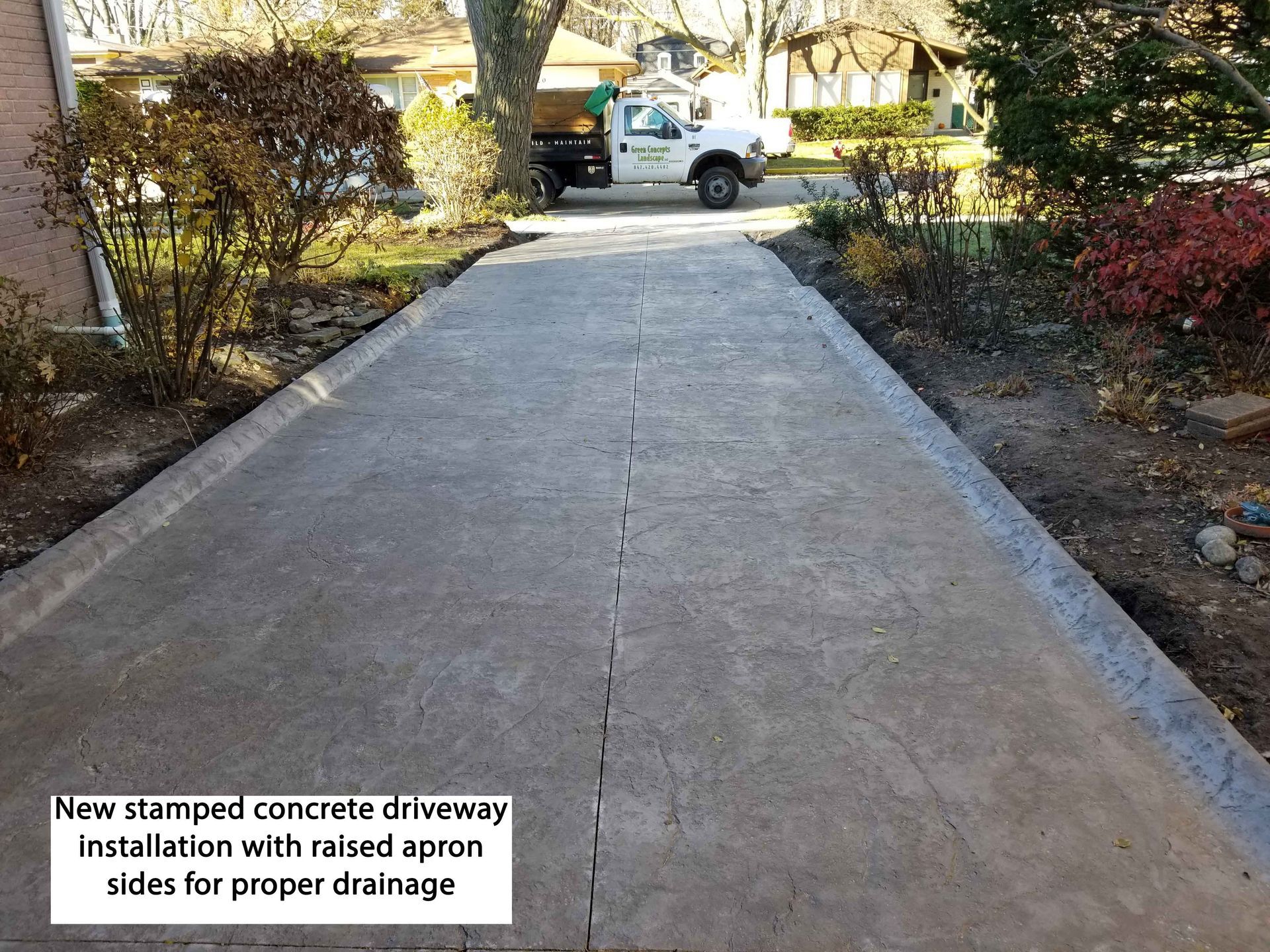 Stamped concrete driveway with raised sides for drainage, with a truck in the background.
