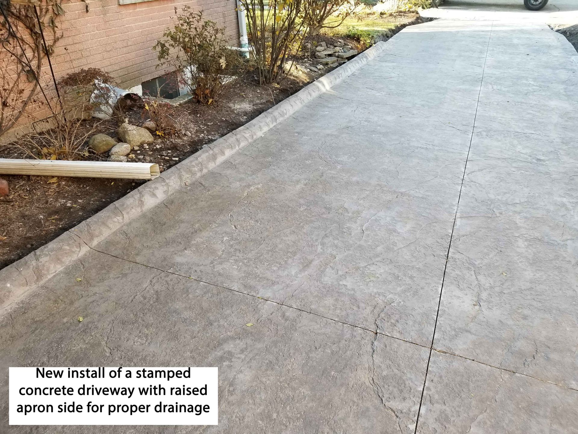 Concrete driveway with raised side, for drainage. Text: New install of stamped driveway.