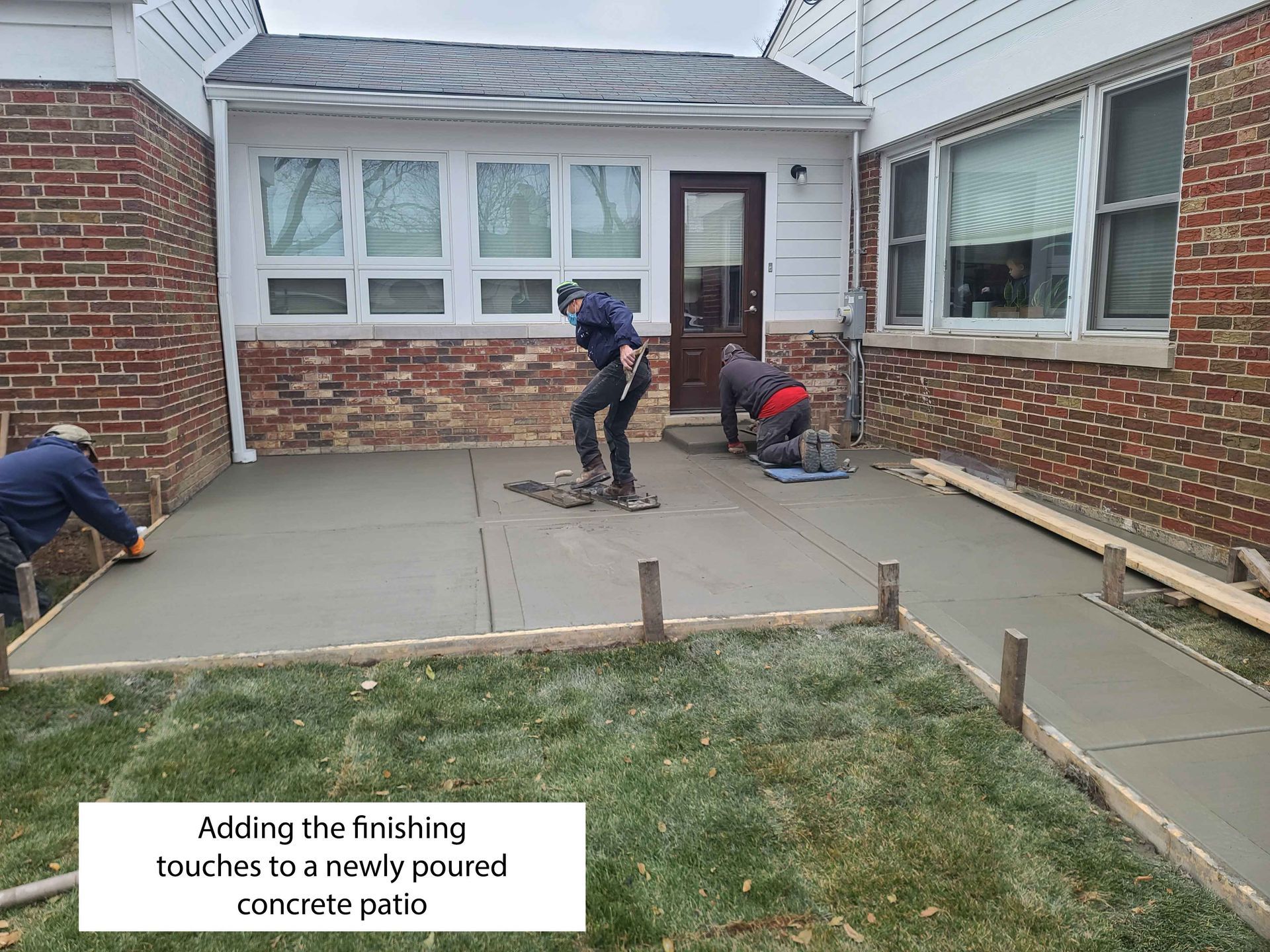 Workers finishing a newly poured concrete patio near a brick building.