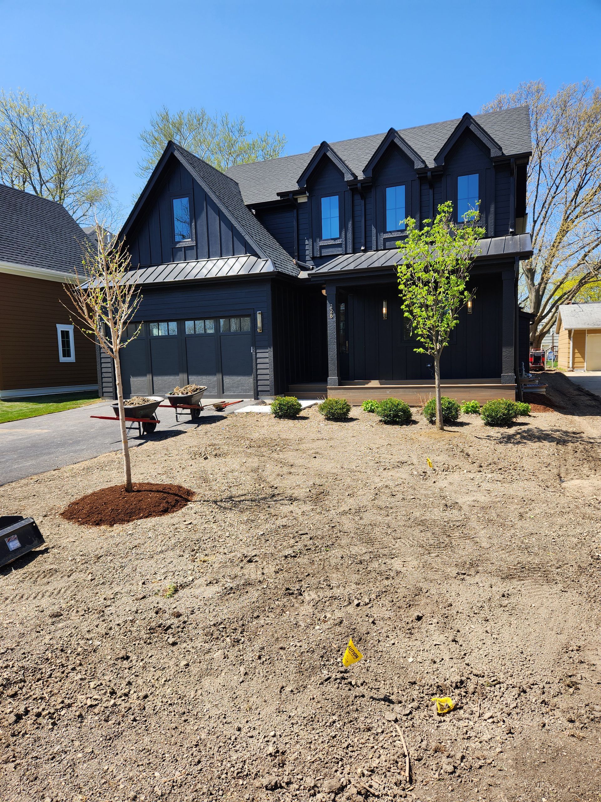 Black modern house with garage and dormers; new lawn, trees, blue sky.