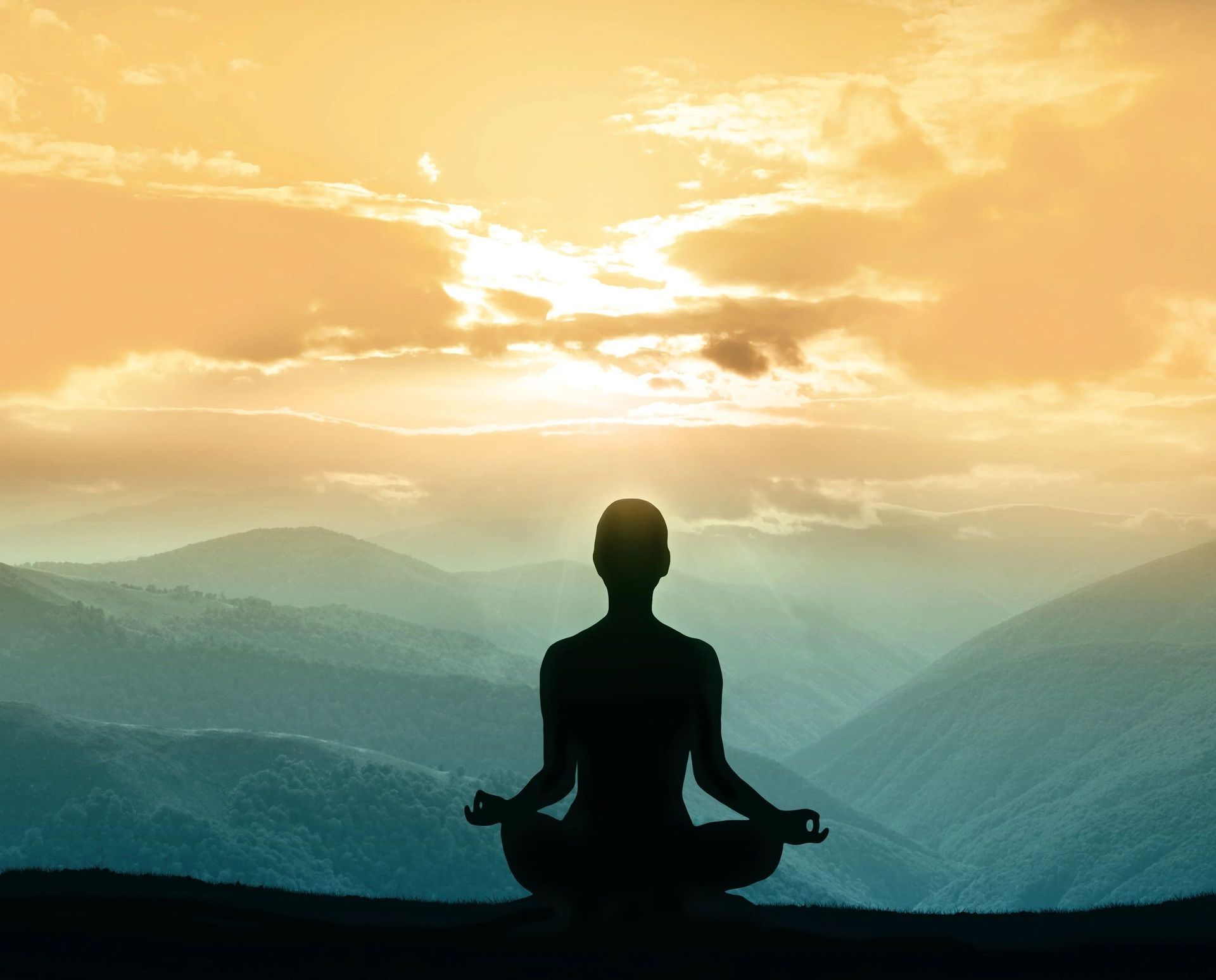 Silhouette of person meditating on a mountain, overlooking a landscape, against a sunset sky.