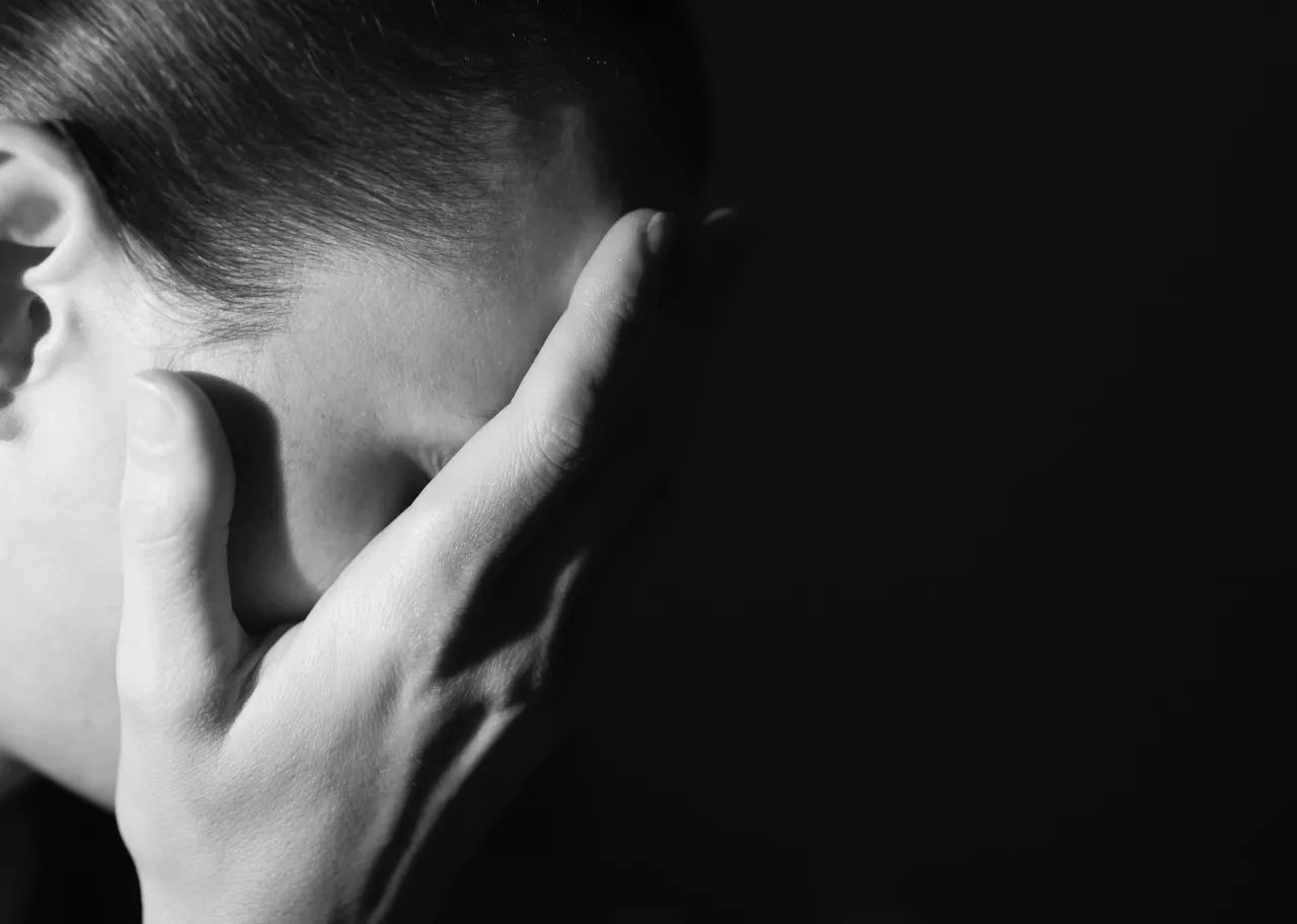 Hand covering the side of a head, dark background.