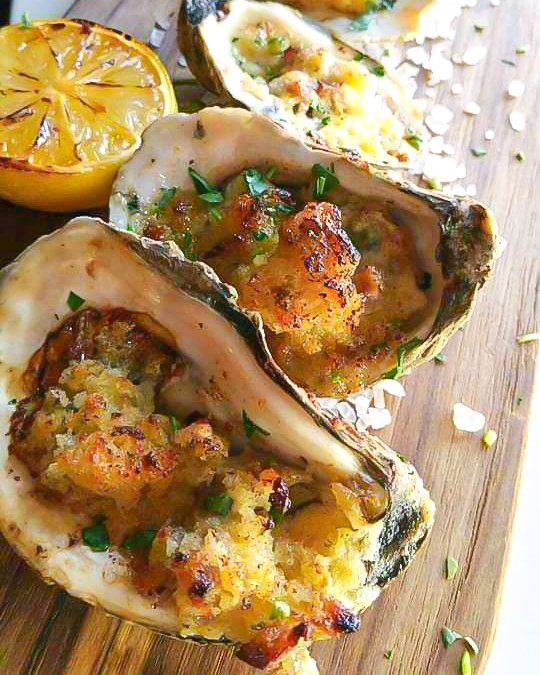 Three oysters are sitting on a wooden cutting board with a slice of lemon.