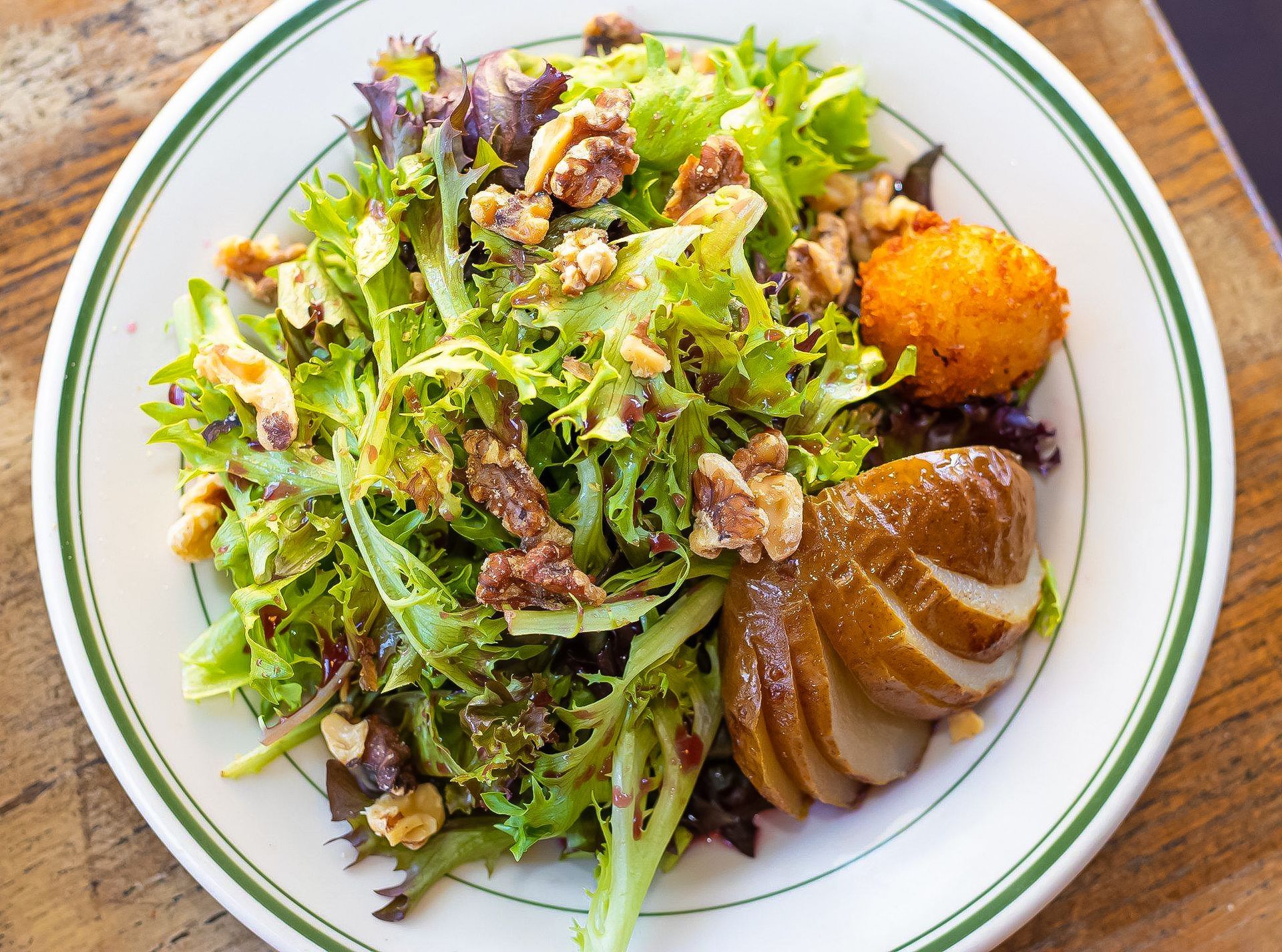 A white plate topped with a salad and a piece of meat on a wooden table.