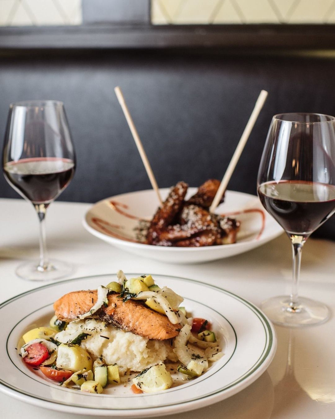 Two plates of food and two glasses of wine on a table