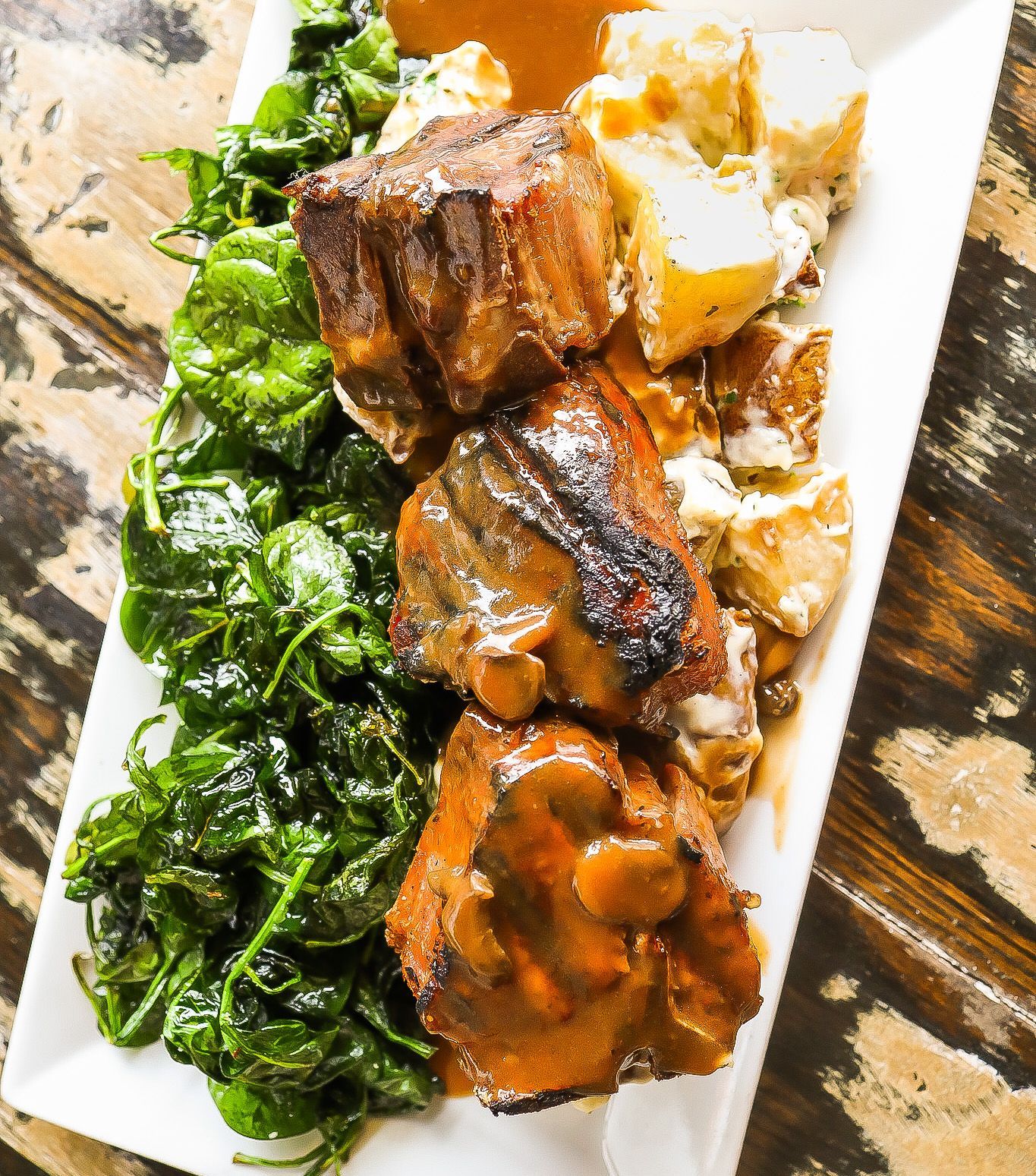 A white plate topped with meat and spinach on a wooden table