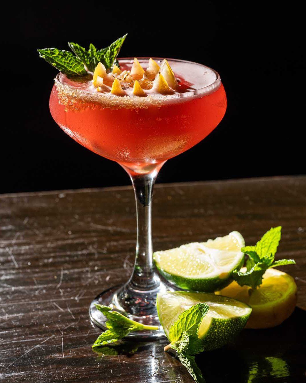 A close up of a red cocktail in a martini glass on a wooden table.