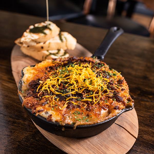 A skillet filled with food is on a wooden cutting board