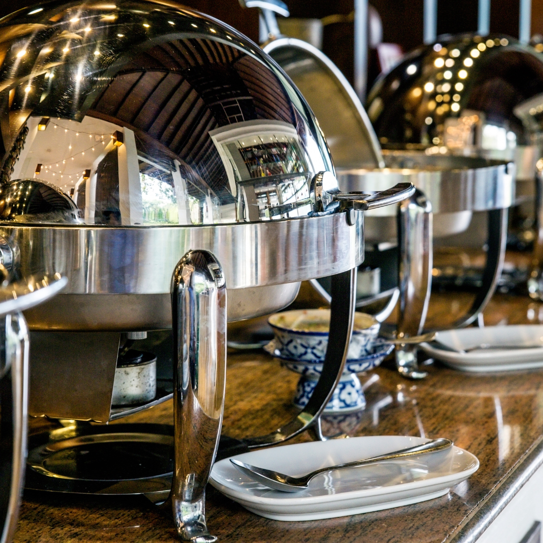 A row of stainless steel chafing dishes are lined up on a counter.