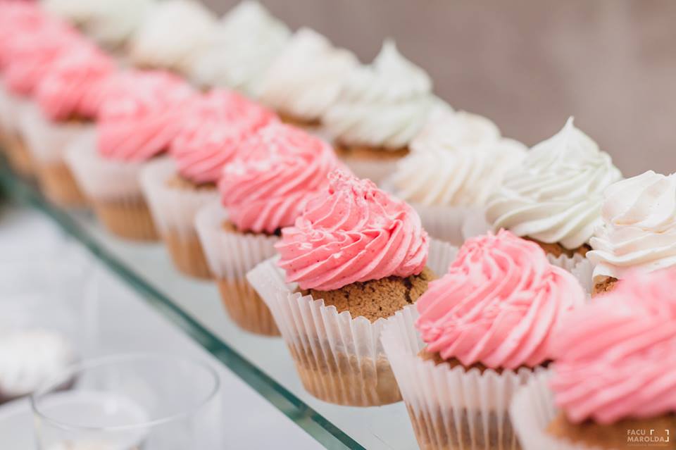 Una fila de pastelitos con glaseado rosa y blanco en un estante de vidrio.