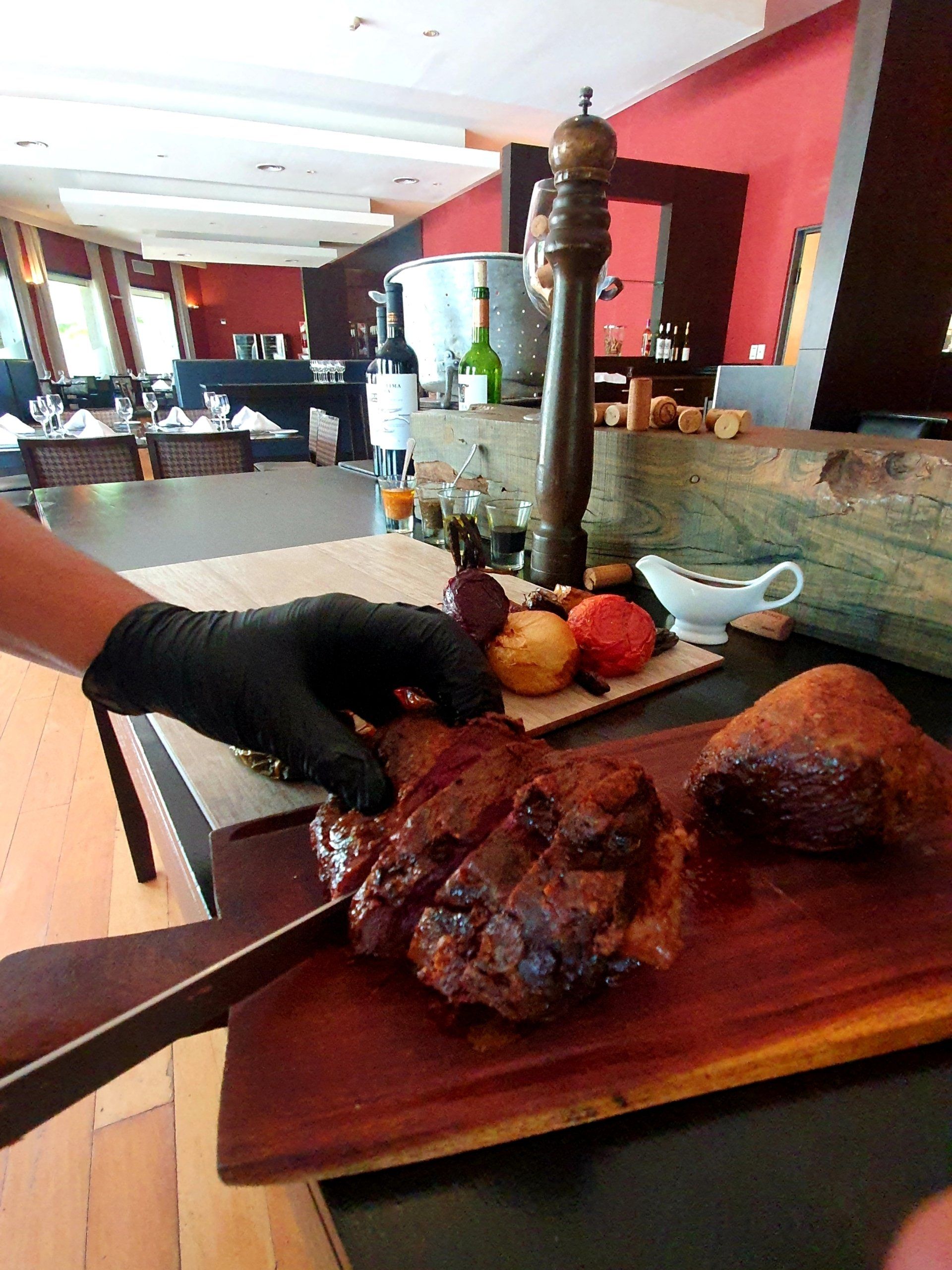 Manos con guantes cortando carne asada