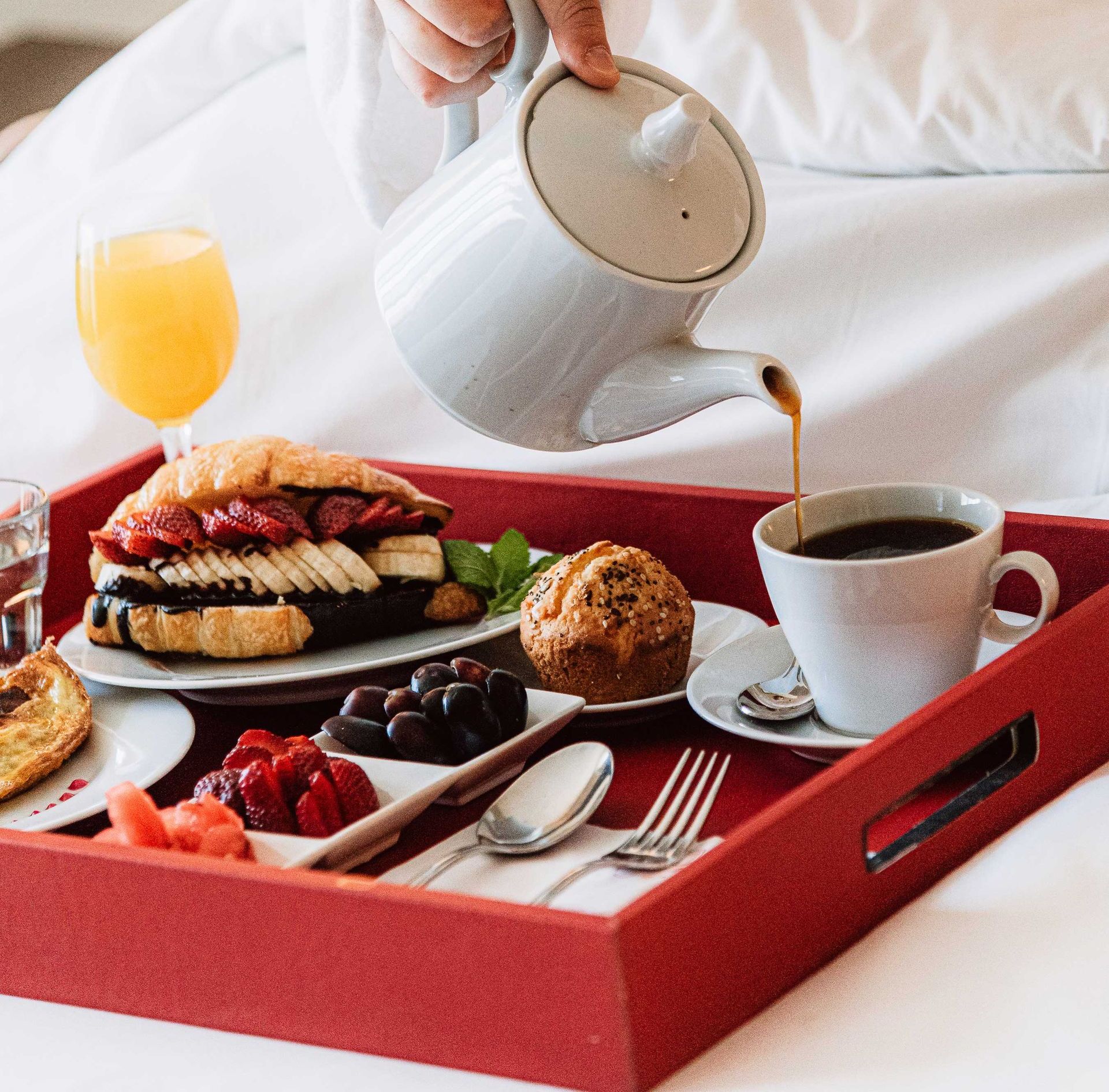 Una persona sirviendo café en una taza sobre una bandeja de comida