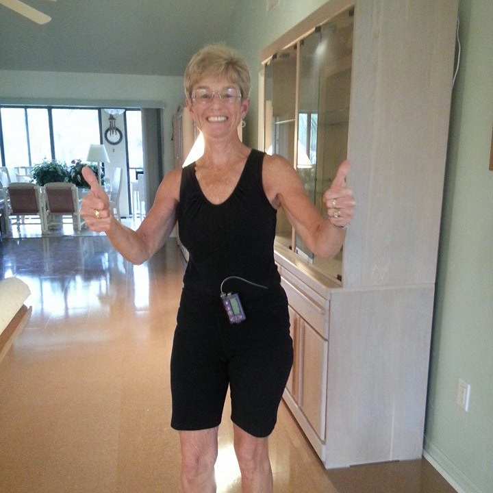 Woman in black workout clothes giving thumbs up; in a home with a cabinet.