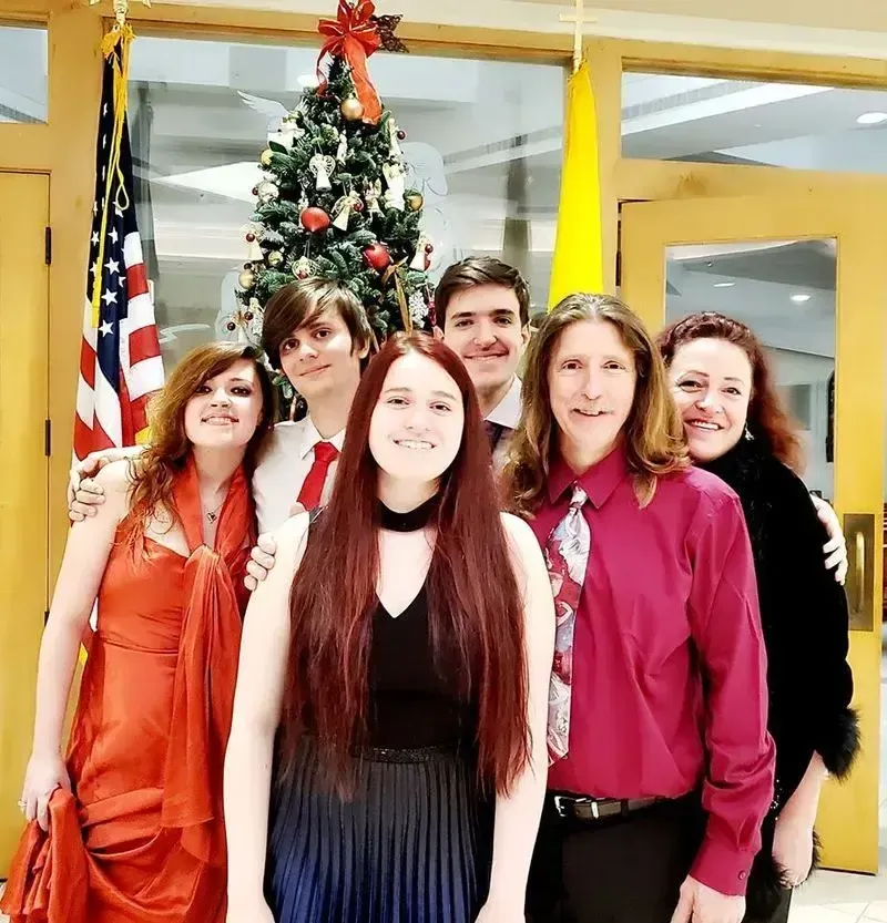 A group of six family members posing together indoors in front of a decorated Christmas tree and an American flag.