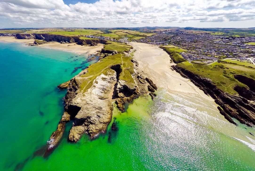 Aerial view of scenic coastline with green cliffs, sandy beaches, and turquoise waters extending to a town.