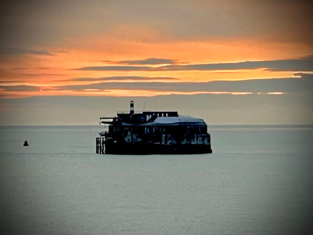 Silhouette of an offshore fort against a vibrant orange sunset, with calm waters and a distant buoy.