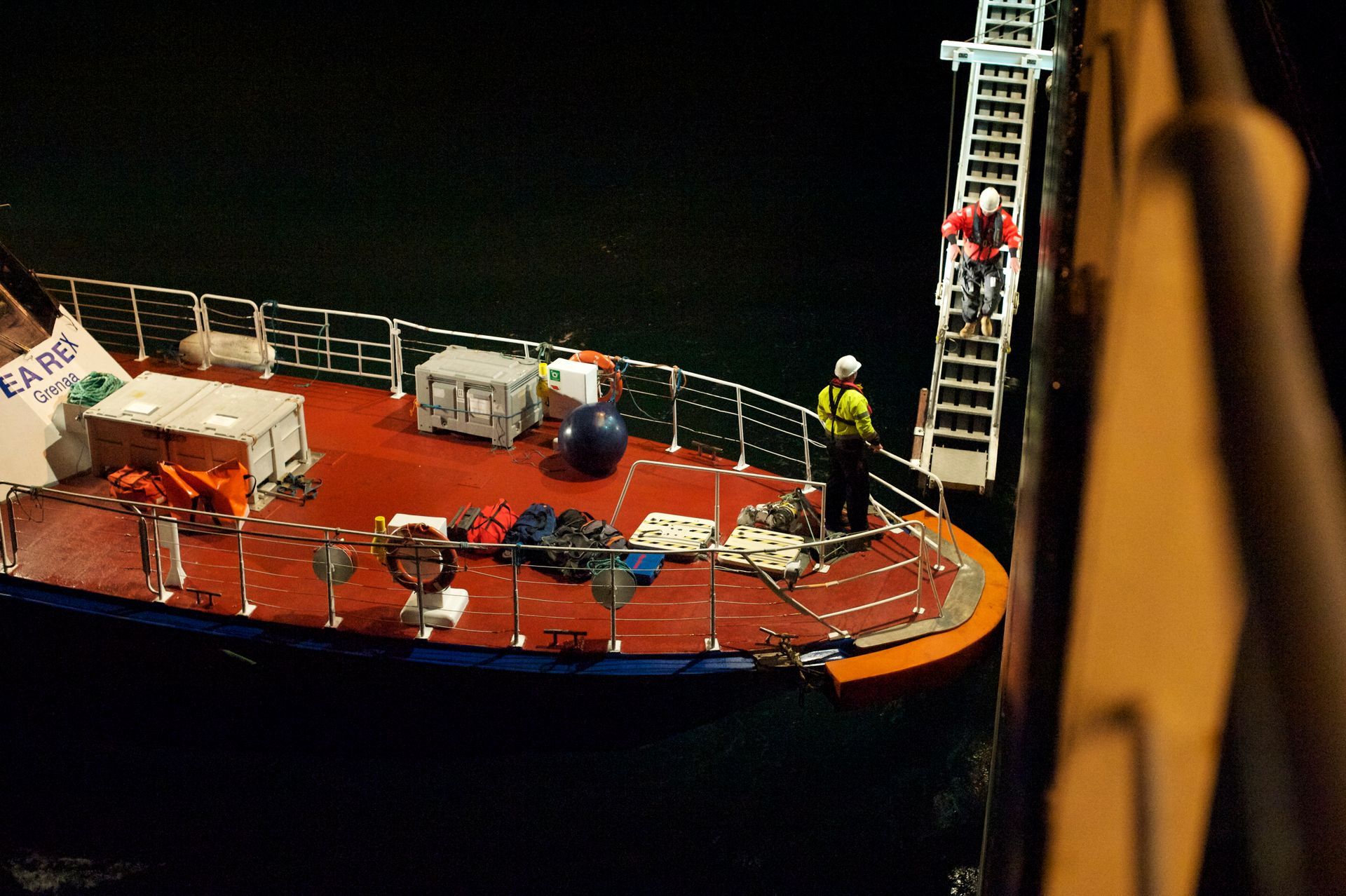 Nighttime scene of crew members on a supply vessel transferring equipment and personnel to a larger offshore platform